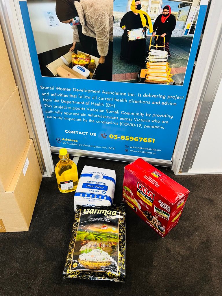 Culturally appropriate groceries including basmati rice, flour, pasta and oil beside an SWDA food relief banner